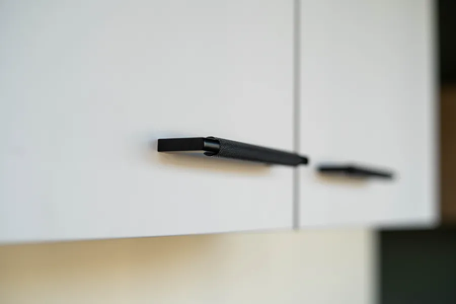 Een close-up van een witte kast met zwarte handgrepen in een keukenkantoor.