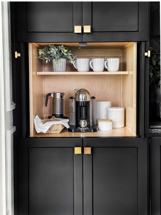 Een zwart kastje met een koffiezetapparaat en mokken, perfect voor een keukenkantoor.